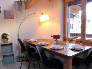 A dining area with a wooden table set for four, a floor lamp, and a view of the street through a window.