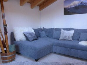 A corner living room with a blue sectional sofa, a white fluffy throw, and a painting of a mountain landscape.