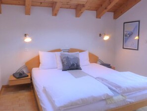 A bedroom with a wooden ceiling, a bed with white bedding, two bedside tables, and a framed picture on the wall.