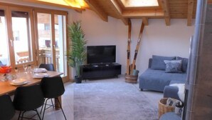 A cozy living area with a sofa, TV, and dining setup with chairs and a table. - Arbgrat by Interhome (Täsch)