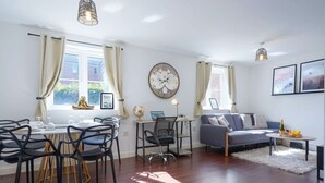 A modern living room with a dining area, a sofa, a coffee table, and a clock on the wall. - Beautiful Apartment • Close to Town Centre • Free Parking • Fast-Wifi • Sky TV • By Yoko Property (Northampton)