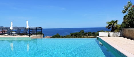 A clear blue pool with lounge chairs and umbrellas, overlooking a scenic ocean view.