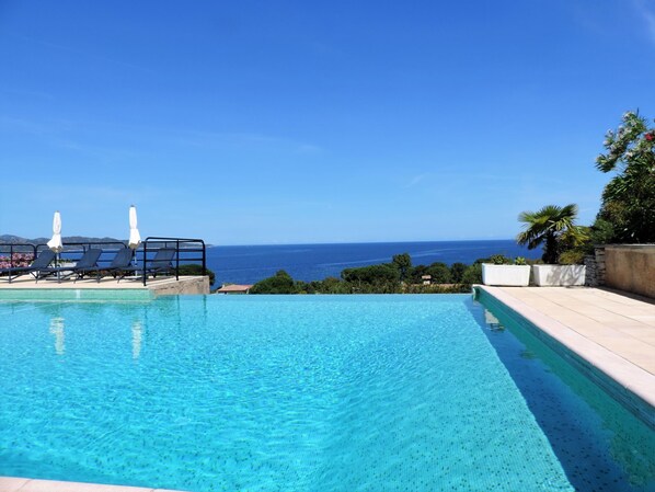 A clear blue pool with lounge chairs and umbrellas, overlooking a scenic ocean view.