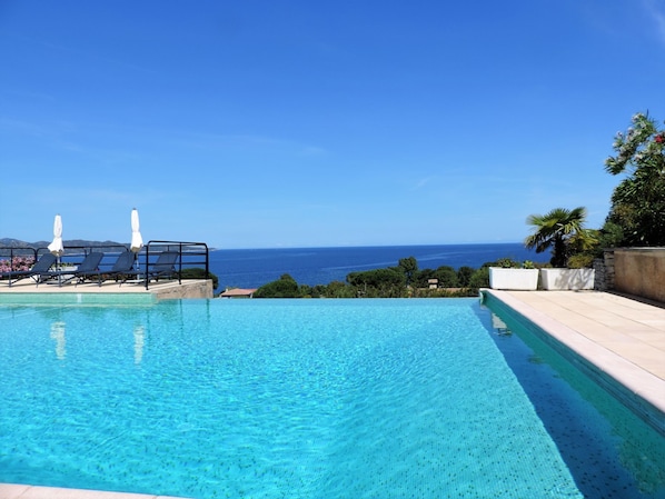 A clear blue pool with lounge chairs and umbrellas, overlooking a scenic ocean view.