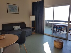 Una sala de estar con sofá, una mesita, una lámpara y vistas a un balcón exterior con mesa y sillas.