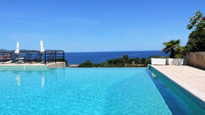 A clear blue pool with lounge chairs and umbrellas, overlooking a scenic ocean view. - Studio Cabine by Interhome (Saint-Florent)