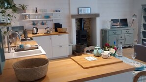 Een gezellige keuken met witte kastjes, een houten aanrecht en een stenen open haard.