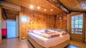 Un dormitorio con paneles de madera, una cama, un ventanal con cortinas de encaje y una pequeña zona de kitchenette.