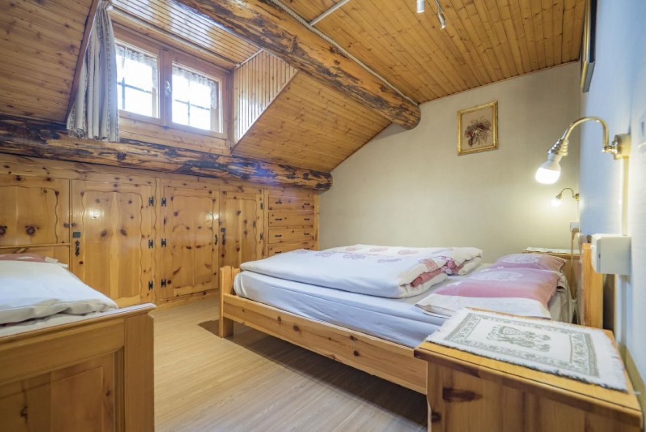 Un dormitorio de cabaña de madera acogedor, con zona de dormir en un altillo, una cama individual, una mesita de noche y un ventanal con cortinas.