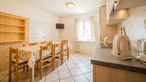 A compact kitchen with a dining area, wooden cabinets, a built-in TV, and a kettle on the counter. - You'll have everything at your fingertips by staying at Quadrilocale Aprica! (Livigno)