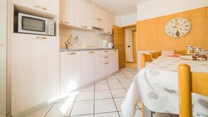 A kitchen with a microwave, wooden cabinets, a clock, and a dining table with chairs. - You'll have everything at your fingertips by staying at Quadrilocale Aprica! (Livigno)