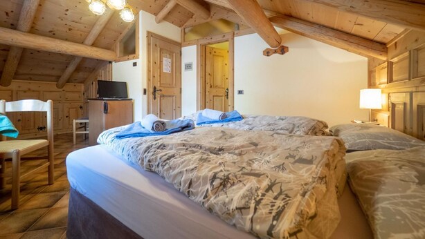 Ein gemütliches Zimmer mit Holzboden, zwei Betten mit gemusterten Bettbezügen, einem Schreibtisch und einem Fernseher.