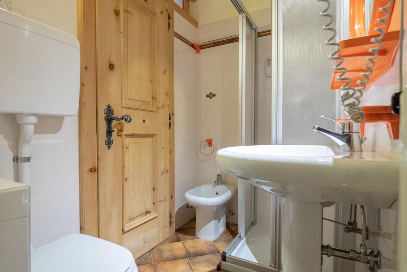 A bathroom with a wooden door, a white toilet, a bidet, and a sink with a glass enclosure.