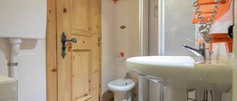 A bathroom with a wooden door, a white toilet, a bidet, and a sink with a glass enclosure.