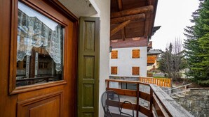 Ein hölzerner Balkon mit Stuhl und Tisch, mit Blick auf ein Gebäude mit Holzhörnern und einer Steinmauer.