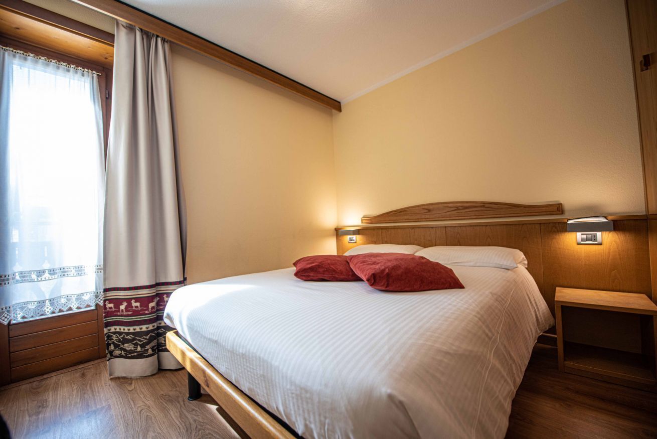 A neatly made bed with a wooden headboard, a bedside table with a lamp, and a window with curtains.