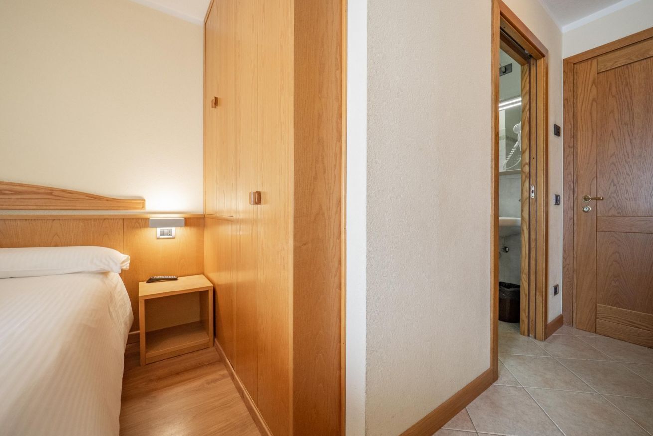 Een hotelkamer met een bed, nachtkastje en een houten garderobe.