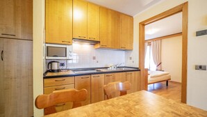A compact kitchen with wooden cabinets, a microwave, and a sink. There is a dining table with chairs and a bed in the adjacent room. - Autonomy, but also comfort? Residence Livigno is the one for you! (Livigno)