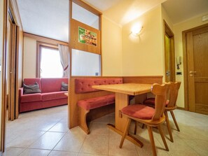 Un coin repas avec une table en bois et deux chaises, un canapé rouge et une fenêtre avec des rideaux.