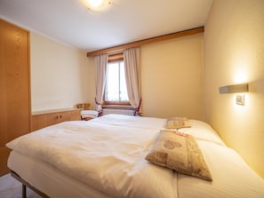Un lit bien fait, avec une tête de lit en bois, une petite table de chevet avec une lampe et une fenêtre avec des rideaux.