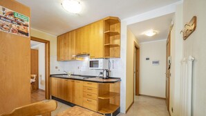 A compact kitchen with wooden cabinets, a microwave, and a sink. There is a dining table with chairs. - Simple, yet traditional. The two-room apartment at Residence Livigno will leave (Livigno)