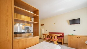 A compact hotel room with a kitchenette, a dining area with a bench, and a TV mounted on the wall. - Simple, yet traditional. The two-room apartment at Residence Livigno will leave (Livigno)