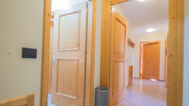 A hallway with wooden doors and a trash can.