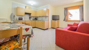 A compact living space with a dining table, a sofa, a television, and a kitchenette.