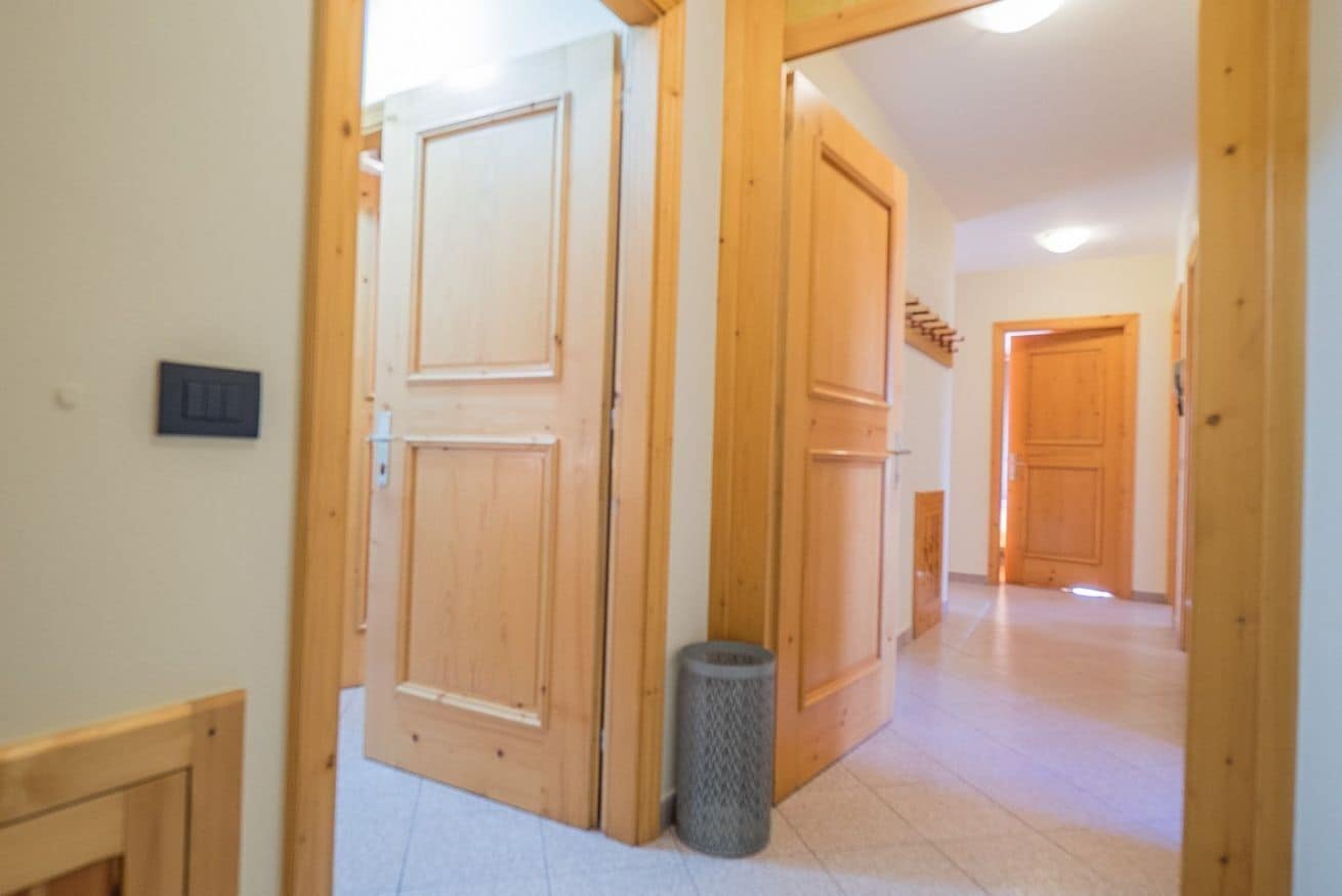 A hallway with wooden doors and a trash can.