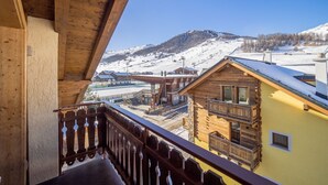 Un balcón de madera con vistas a una montaña nevada y edificios de una estación de esquí.