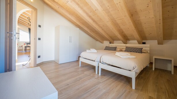 Un dormitorio con techo inclinado, una cama con dos almohadas, una mesita de noche y un armario.