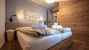 Ein Doppelbett mit weißen Bettwäsche und einer gemusterten Decke, ein Holz-Kopfteil, eine Wandleuchte und ein gerahmtes abstraktes Kunstwerk.
