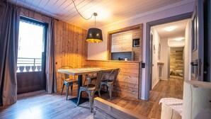 Ein gemütliches Zimmer mit einem Holzespeisetisch und Stühlen, einer Hängeleuchte und Blick in ein Badezimmer durch eine offene Tür.
