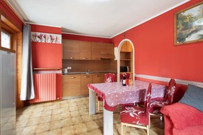 Eine kleine Küche mit Holzausstattung, einem Esstisch mit rot-weißer Tischdecke und einem roten Sofa.