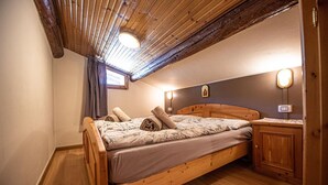 A bedroom with a wooden bed, a nightstand, a wall-mounted lamp, and a ceiling with wooden beams. - Your next stay in Livigno without giving up anything! (Livigno)