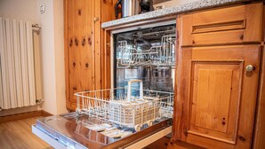 An open dishwasher in a kitchen with wooden cabinets and a white countertop. - Your next stay in Livigno without giving up anything! (Livigno)