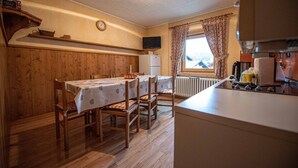 Eine gemütliche Küche mit Holzwänden, einem Esstisch mit Stühlen, einem eingebauten Backofen und einem Fenster mit Vorhängen.