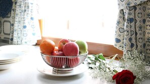 A bowl of fruit on a table near a window with curtains.