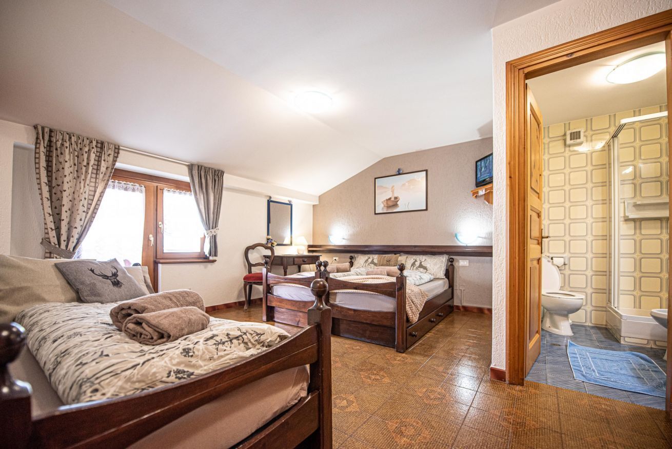 A room with two wooden beds, a wooden dresser, a small table, and a window with curtains.