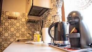 A kitchen with patterned tiles, a coffee maker, a roll of paper towels, and a small bottle.