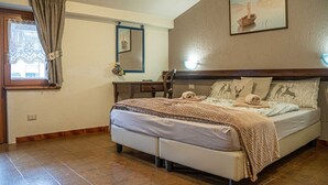 A bedroom with a bed, a desk, a chair, a window with curtains, a mirror, and a painting on the wall.