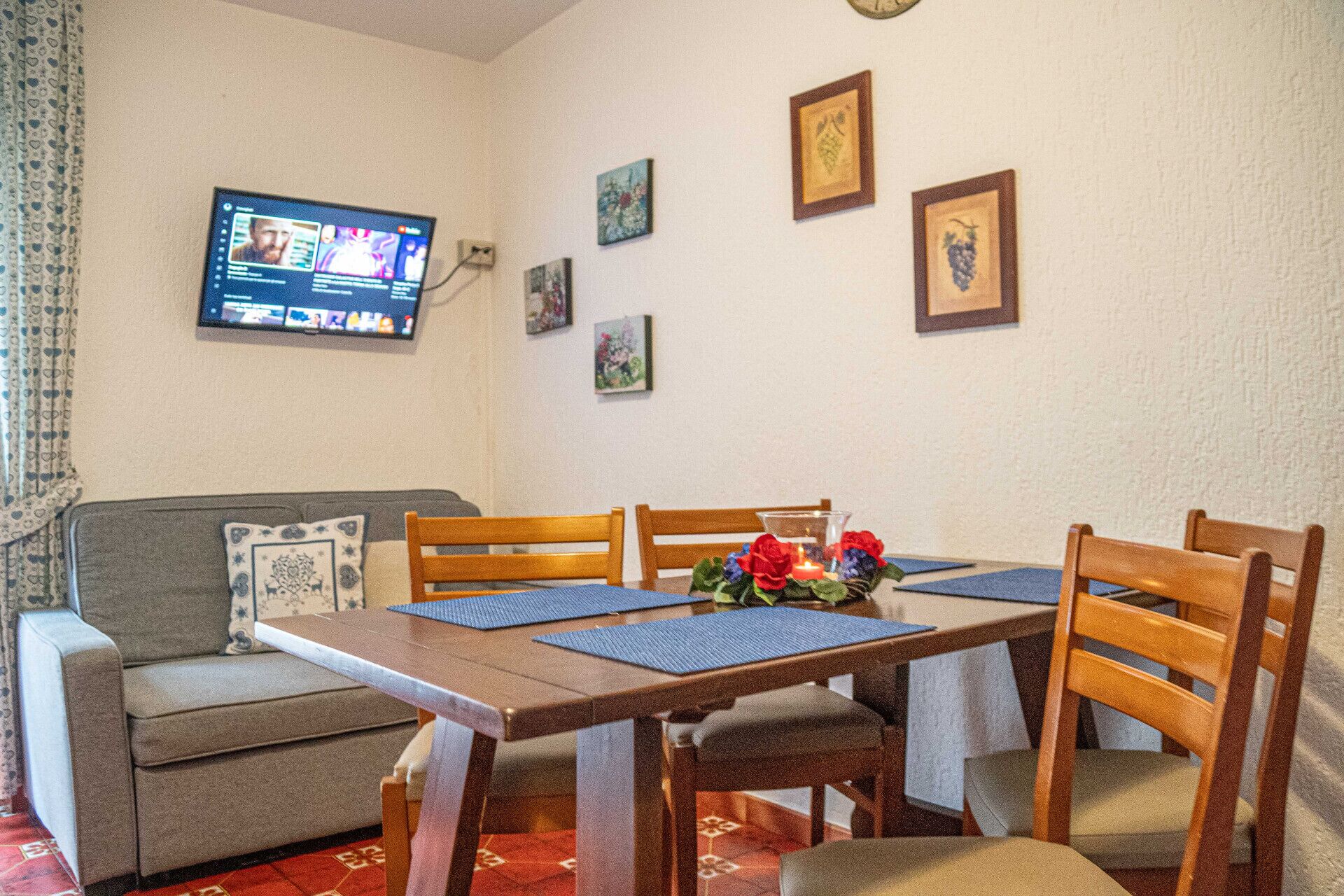 A dining area with a wooden table, four chairs, and a television mounted on the wall.