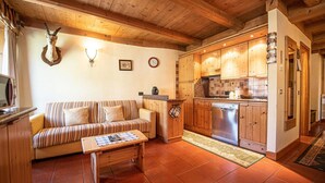 Una sala de estar acogedora con un sofá a rayas, una mesa de centro de madera y una cocina con armarios de madera y un lavavajillas de acero inoxidable.