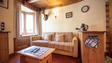 Ein gemütliches Wohnzimmer mit einer gestreiften Couch, einem Holztisch und einer Küchenzeile mit Wasserkocher und Backofen.