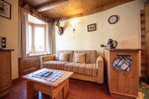 Una sala de estar acogedora con un sofá a rayas, una mesa de centro de madera y un área de cocina con hervidor y horno.