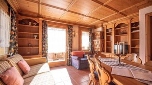 Un salon chaleureux avec un plafond en bois, un canapé agrémenté de coussins à rayures, une table à manger avec des chaises et une bibliothèque remplie de livres et d’objets décoratifs.