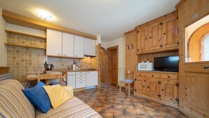 Una sala de estar acogedora con un sofá a rayas, una mesa de comedor de madera y una zona de cocina con armarios de madera y un microondas.