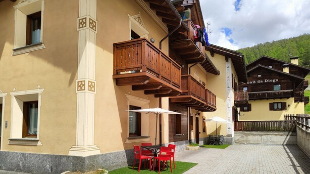 A building with a wooden balcony, outdoor seating with red chairs, and a paved courtyard. - The Real Wood Chalet awaits you for a vacation in comfort. (livigno)