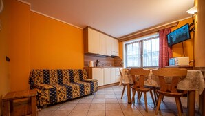 A compact living space with a sofa, dining table, chairs, a kitchen area, and a TV mounted on the wall. - Enjoy your next vacation in Livigno at Chalet Amalia (Livigno)