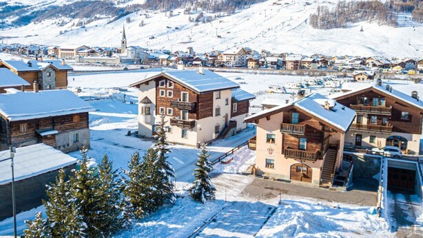 Un village enneigé, avec ses maisons traditionnelles en bois, une église et, au loin, une piste de ski.